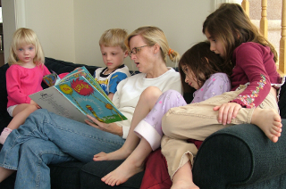 [Several children sitting on a sofa with their mother, reading a book together.]