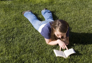 [teenager reading, on a grassy lawn]